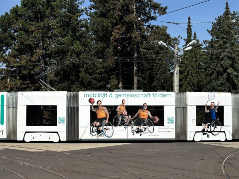 Rollstuhlsportler auf Straßenbahn-Fensterseite mit Bandagist-Heindl-Logo und Aufschrift 
